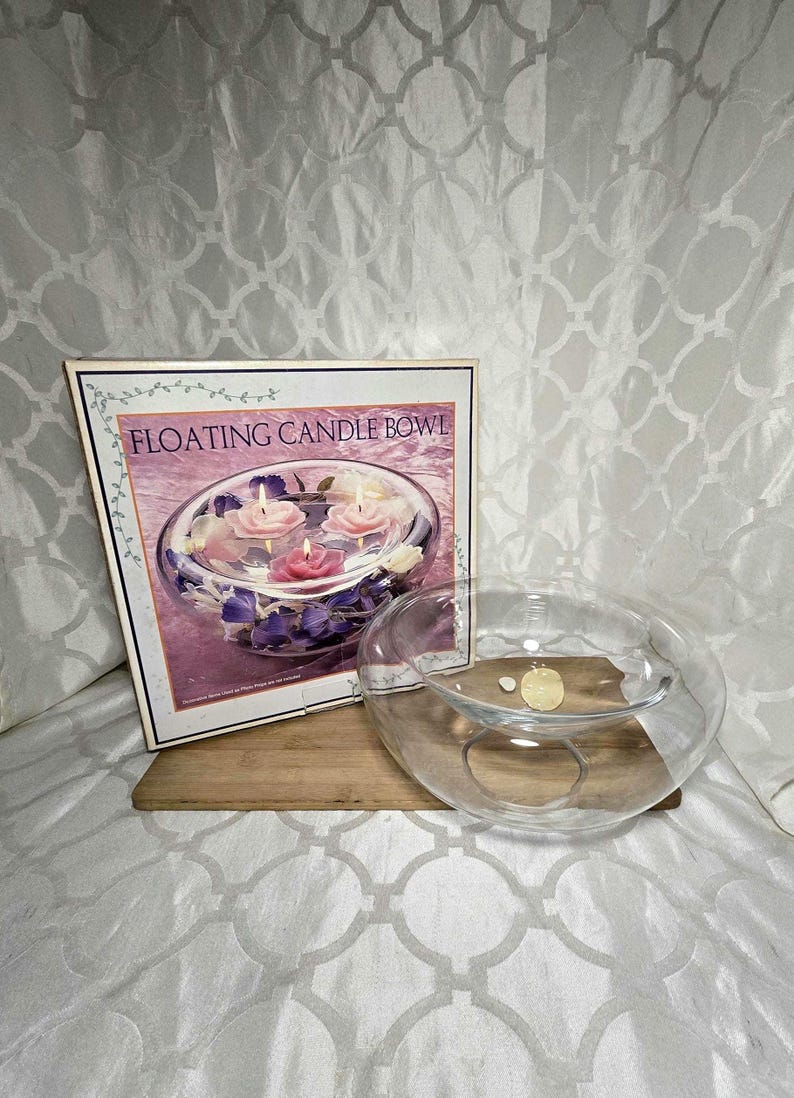 May include: A clear glass floating candle bowl with a box that reads "FLOATING CANDLE BOWL". The box shows the bowl with floating candles and floral accents. The bowl sits on a wooden board.