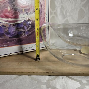 May include: A clear glass decorative bowl with a unique design. The bowl is approximately 8 inches in diameter. The bowl is on a wooden surface. A measuring tape is next to the bowl.