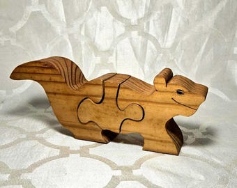 May include: A wooden squirrel puzzle with three interlocking pieces. The squirrel is light brown with visible wood grain and a smiling face. The tail and back have detailed wood grain patterns. A fun, educational toy.