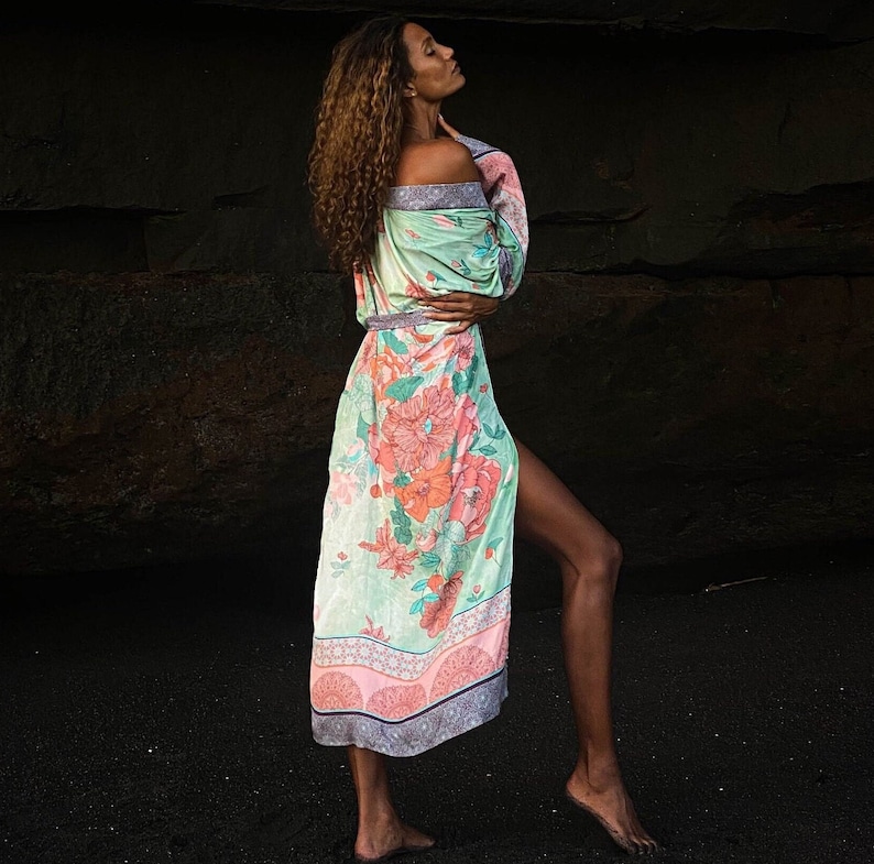 May include: A woman wearing a long, flowing green and pink floral print robe with a side slit. The robe has a delicate floral pattern and a pink and white trim.