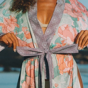 May include: A light green and purple floral print kimono with a tie sash. The kimono has a light pink floral pattern with green leaves.