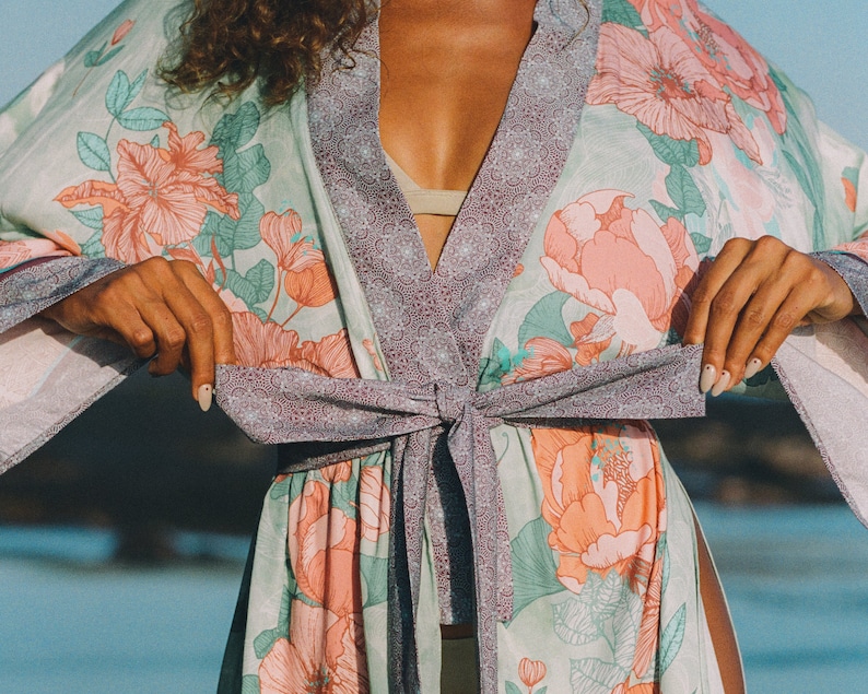 May include: A light green and purple floral print kimono with a tie sash. The kimono has a light pink floral pattern with green leaves.