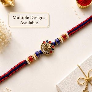 Op de afbeelding: Een decoratieve armband met een centrale goudkleurige bedel met een Om-symbool, omringd door rode en blauwe blaadjes en heldere kristallen. De band is gemaakt van gevlochten rode en blauwe draden, geaccentueerd met gefacetteerde kralen en kleine witte parels. Tekst: Multiple Designs Available.