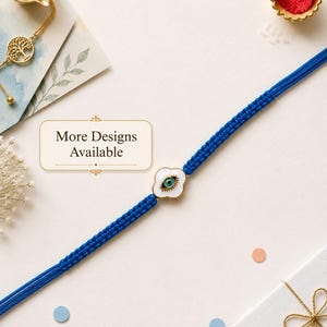 Könnte beinhalten: Ein blaues geflochtenes Armband mit einem mittigen, kleeblattförmigen weißen Anhänger, der ein blau-schwarzes Auge-Motiv zeigt. Ein rechteckiges Schild mit dem Text More Designs Available befindet sich neben dem Armband auf hellem Grund.