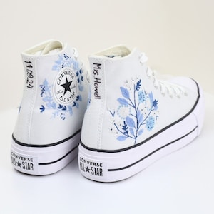 May include: White high-top Converse sneakers with blue floral embroidery. The left shoe has the text "11.09.24" on the side and the right shoe has the text "Mrs. Howell" on the side.