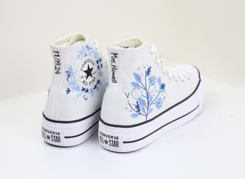 May include: White high-top Converse sneakers with blue floral embroidery. The left shoe has the text "11.09.24" on the side and the right shoe has the text "Mrs. Howell" on the side.