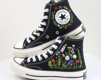 May include: Black high-top sneakers with white laces and soles. The sneakers feature floral embroidery and the Converse All Star logo. The embroidered flowers include red, pink, orange, and blue.