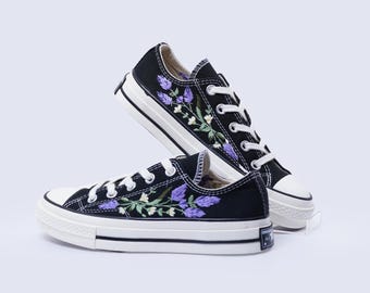 May include: Black canvas low-top sneakers with white soles and purple floral embroidery.
