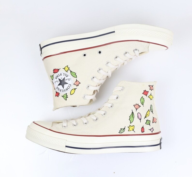 K&ouml;nnte beinhalten: Wei&szlig;e Converse-Sneaker mit hohem Schaft, floralem Muster und schwarzem Stern-Logo. Der Schriftzug "Converse All Star" ist an der Seite des Schuhs aufgedruckt.