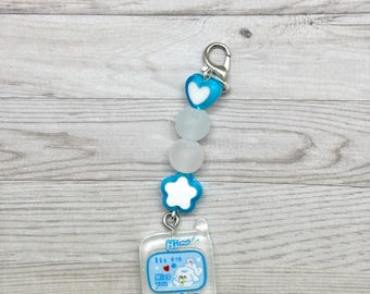May include: A clear, glittery phone charm with a blue and white design. The charm features a small phone with the text "Miss You" and a cartoon character. It is connected to a chain with blue heart and star-shaped beads, and frosted white beads.