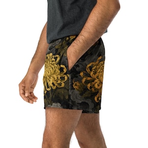 May include: Athletic shorts featuring a dark charcoal gray background with a repeating pattern of large, golden-yellow chrysanthemum flowers and muted gray foliage. The shorts include a side pocket and are paired with a dark gray t-shirt.
