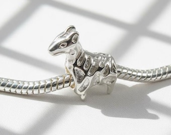 May include: A silver charm in the shape of a small animal, possibly a rodent, is centered on a silver chain. The charm has detailed features and a textured surface. The background is white with shadows.