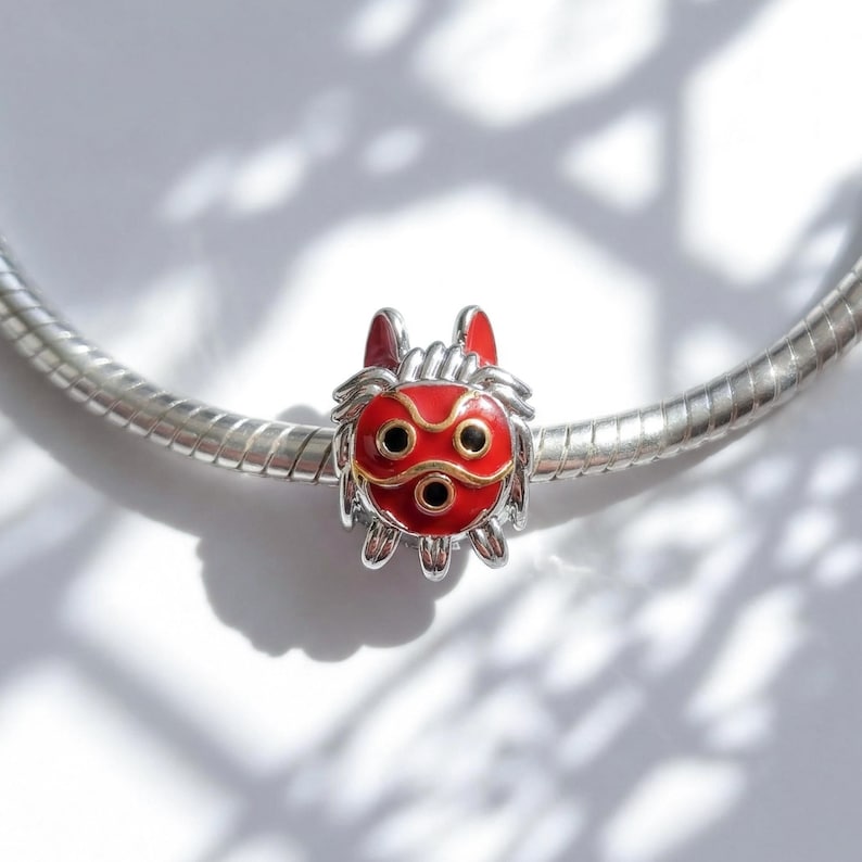 Pu&ograve; includere: Un charm rosso e argento con un design dettagliato. Il charm presenta una maschera rossa con dettagli dorati e dettagli neri per occhi e bocca. Il charm &egrave; attaccato a un braccialetto d'argento.