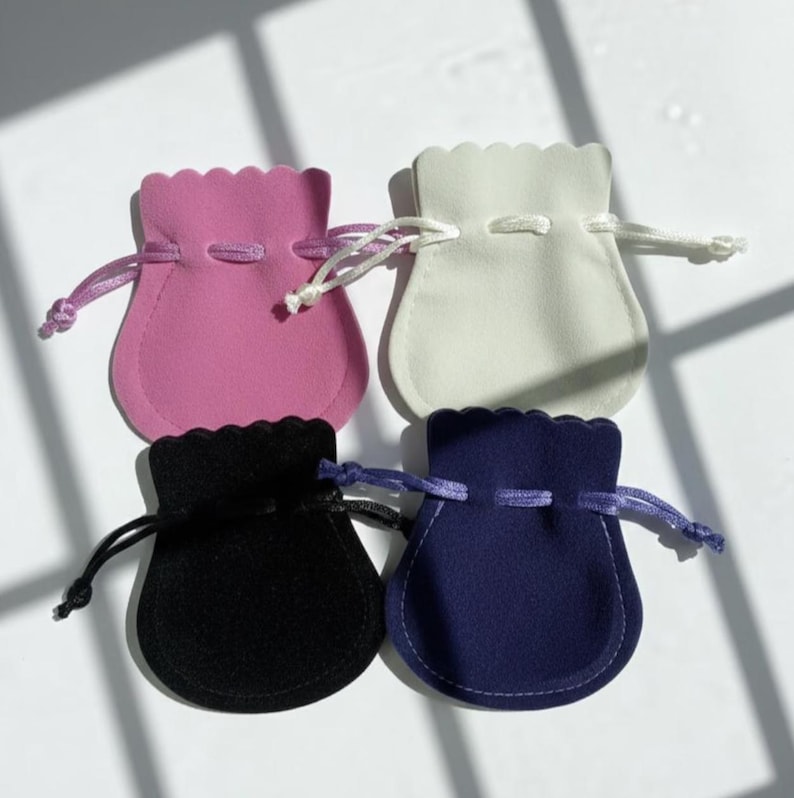 Pu&ograve; includere: Quattro piccole bustine con coulisse rosa, bianche, nere e blu navy. Ogni bustina ha un bordo superiore smerlato e una chiusura con coulisse abbinata. Le bustine sono realizzate in un materiale morbido e vellutato e sono disposte su una superficie bianca.