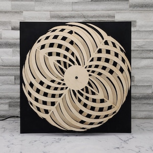 May include: Abstract wooden wall art with a circular design. The artwork features layered, curved elements in light wood against a black background. The symmetrical design creates a striking contrast. The piece is suitable for interior decoration.