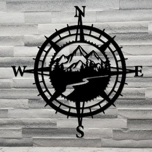 Peut inclure: Boussole en métal noir avec un motif de montagne et de rivière. La boussole indique le nord, le sud, l'est et l'ouest.