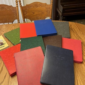 May include: A collection of ten magazine binders in various colors, including red, green, blue, brown, and black. Each binder has the text "MAGAZINE FOLDER" embossed on the front.