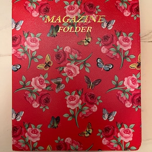 May include: A red magazine folder featuring a repeating pattern of pink and dark red roses with green leaves and various colorful butterflies. The words MAGAZINE FOLDER are printed in gold lettering in the center of the front cover.