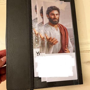 May include: A black leather-bound journal with a clear plastic pocket on the front cover. The pocket contains a printed image of a man with a beard and long hair, wearing a white robe and a red sash. The image is titled "You Are My"
