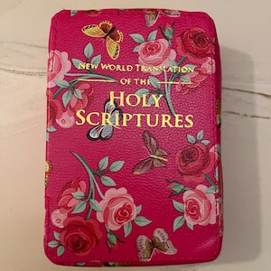 May include: A hot pink Bible with a floral and butterfly pattern. The cover features roses and butterflies in shades of pink, red, and yellow. Gold lettering reads "New World Translation of the Holy Scriptures."
