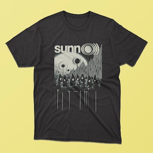 May include: Black t-shirt with a white graphic of a band called "sunnO". The graphic features a stylized moon with a circle around it, mountains, and figures in hooded robes.