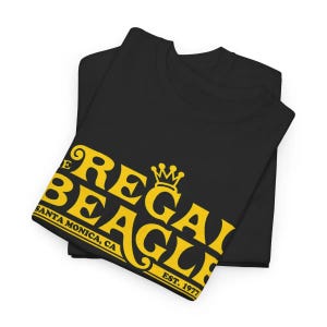 Może przedstawiać: Czarny T-shirt z żółtym nadrukiem z napisem "The Regal Beagle" z koroną nad słowem "Regal" i tekstem "Santa Monica, CA Est. 1977" poniżej.