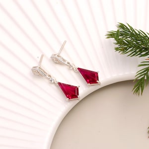 May include: A pair of silver dangle earrings with a red gemstone and clear cubic zirconia accents.
