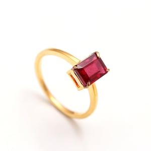 May include: A gold ring with a red emerald-cut gemstone.