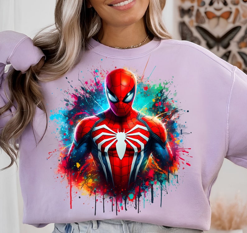 Puede incluir: Una sudadera de color lavanda con un estampado gr&aacute;fico colorido de Spider-Man con un traje rojo y negro. El gr&aacute;fico tiene un efecto de pintura salpicada.