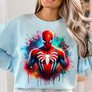 Puede incluir: Una sudadera azul claro con un dise&ntilde;o de salpicaduras de pintura de colores con un gr&aacute;fico de Spiderman rojo y negro.