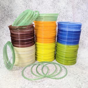 May include: A collection of colourful bangles in shades of green, brown, yellow, orange, and blue. The bangles are made of a translucent material, and some are stacked while others are scattered. The image is well-lit, showcasing the vibrant colours and textures.