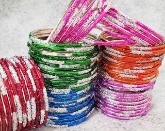 May include: Stacks of colorful bangles in red, green, blue, orange, and pink. Each bangle is metallic and adorned with a silver glitter design. The bangles are stacked in neat piles, showcasing their vibrant colors and decorative details.