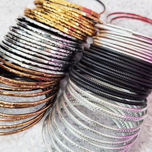 May include: A collection of stacked bangles in various metallic finishes, including gold, silver, and black. Some bangles have textured surfaces, while others are smooth. The bangles are arranged in neat stacks, showcasing their different designs and colors.