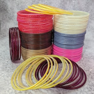 May include: A collection of colorful bangles in various shades, including red, pink, gold, brown, yellow, and purple. The bangles are stacked and arranged, showcasing their different colors and textures. Some are stacked, while others are scattered.