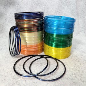 May include: A collection of colourful bangles in shades of blue, green, yellow, orange, and clear. Some bangles are stacked, while others are separate. The bangles are made of a shiny material.