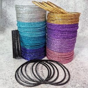 May include: Stacks of glittery bangles in silver, teal, purple, pink, and gold. A separate stack of black bangles is also present. The bangles are arranged in neat stacks, showcasing a variety of colors and textures, perfect for accessorizing.