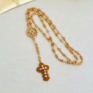 Peut inclure: Chapelet doré avec un pendentif en forme de croix décorative et une pochette assortie. Le chapelet est composé de petites perles rondes et d'une croix détaillée. La pochette est carrée avec une fermeture à ruban.