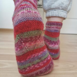 May include: A pair of hand-knitted socks with a vibrant mix of colors, including red, pink, purple, and green stripes. The socks are made of soft yarn and appear to be warm and cozy, perfect for cold weather.