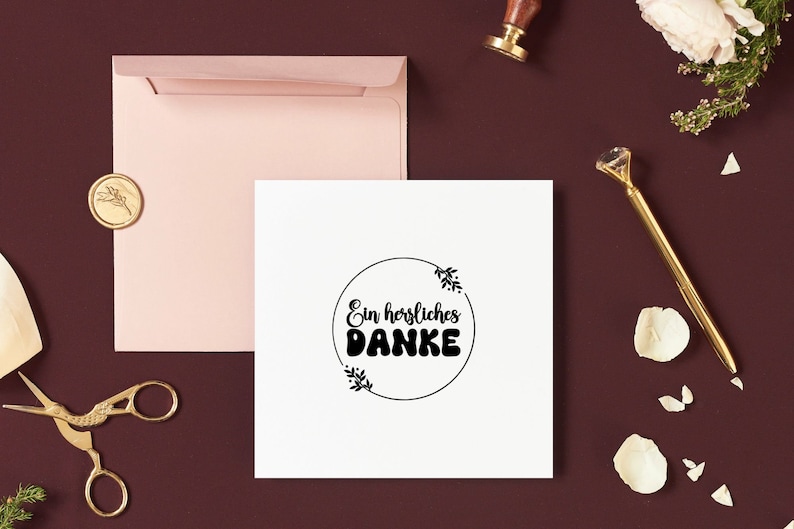 K&ouml;nnte beinhalten: Eine wei&szlig;e Karte mit einem schwarzen Kreis und dem Text "Ein herzliches DANKE" im Kreis. Die Karte ist von einem rosa Umschlag und einem goldenen Siegelwachs umgeben.