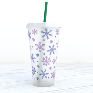 May include: A white reusable cup with a green straw. The cup has a snowflake pattern in shades of purple and blue.