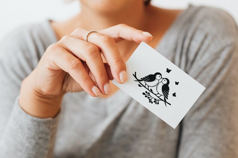 May include: A white card with a black silhouette of two birds perched on a branch with a small cluster of berries. Three small butterflies are also depicted on the card.