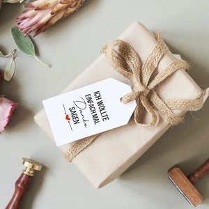 K&ouml;nnte beinhalten: Eine braune Geschenkbox, die in braunes Papier eingewickelt ist, mit einer Schleife aus Juteschnur und einem wei&szlig;en Geschenkanh&auml;nger. Der Geschenkanh&auml;nger tr&auml;gt den Text "Ich wollte einfach mal Danke sagen" mit einem roten Herzen.