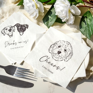 May include: White paper napkins featuring black line drawings of dogs. One napkin has two dog portraits and the text "Drinks on us!" and "Love, Mosh & Ted." Another napkin has a dog portrait and the text "Cheers!" and "Love, Goose."