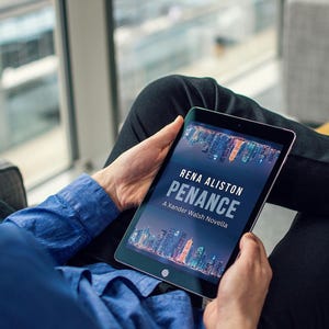 May include: A person holding a tablet displaying the book cover for "Penance" by Rena Aliston. The cover features a cityscape with a dark blue background. The person is wearing a blue shirt and black pants.