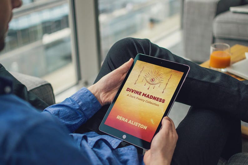 May include: A person holding a tablet displaying the book cover of "Divine Madness: A Dark Poetry Collection" by Rena Aliston. The cover features an eye illustration and text on a yellow and red background. The person is wearing a blue shirt.