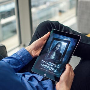 Op de afbeelding: Een tablet toont de boekomslag van "Shadows Mirrors: A Dark Poetry Collection" van Rena Aliston. De omslag toont een portret van een vrouw in een donker kader. De persoon draagt een blauw overhemd en een zwarte broek.