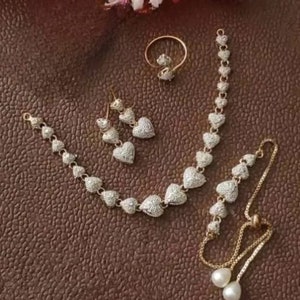May include: A gold-tone jewelry set with a necklace, bracelet, earrings, and ring. Each piece features a heart-shaped design with clear sparkling stones.