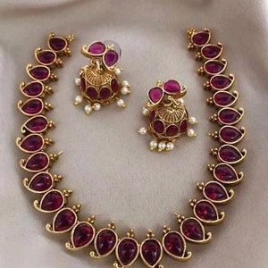 Può includere: Una collana d'oro con un designo a forma di lacrima. Il ciondolo è incastonato con una pietra preziosa rosa scuro ed è circondato da piccoli accenti dorati. La collana è abbinata a orecchini coordinati.