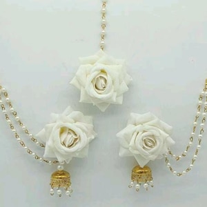 Peut inclure: Un ensemble de trois accessoires pour cheveux en forme de fleurs blanches avec des chaînes dorées et des accents de perles. Les fleurs sont en tissu et ont une forme de rose réaliste. Les chaînes sont attachées aux fleurs et ont un petit pendentif doré à l'extrémité.