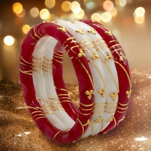 Op de afbeelding: Een set van vier rode en witte armbanden met gouden accenten. De armbanden zijn op elkaar gestapeld en hebben een decoratief ontwerp.